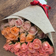Load image into Gallery viewer, Bouquet of pink and peach roses wrapped in brown paper on a wooden surface
