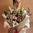 Load image into Gallery viewer, Person holding a bouquet of flowers wrapped in brown paper against a beige background
